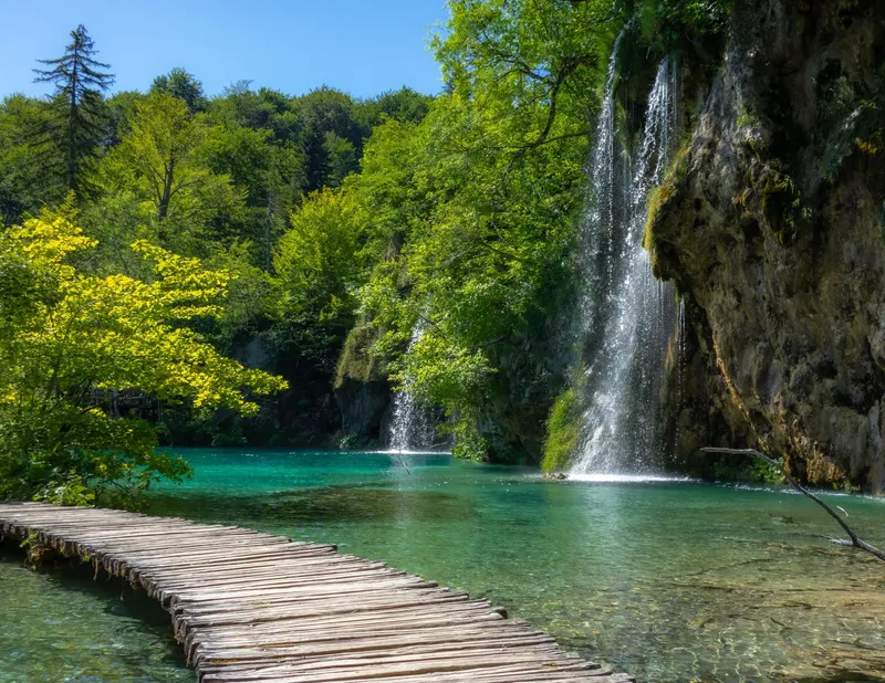 Tropical%20waterfall%20with%20footbridge%0A%20%20%20%20through%20shallow%20water